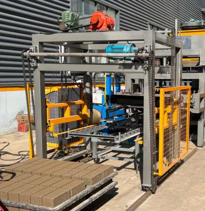 Automatic stacker at the end of the block conveyor, with a pallet of formed blocks below.