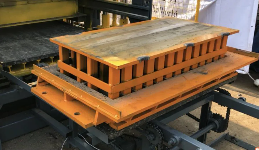 Orange block mould resting on a pallet at the vibration platform during a mould change.