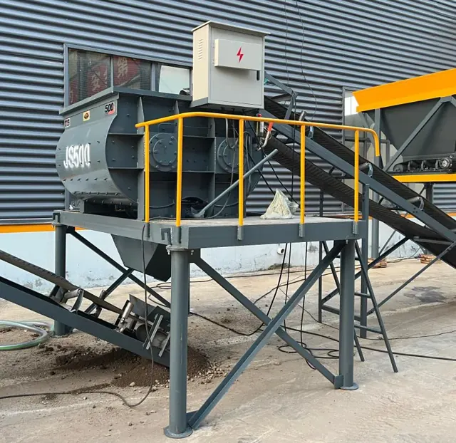 JS500 mixer on steel support legs, with its electrical control box and yellow worker guardrail.